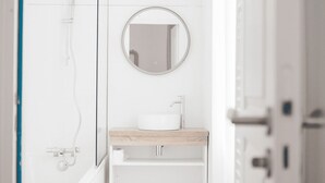 Un baño moderno con lavamanos blanco, espejo redondo y cabina de ducha de vidrio.