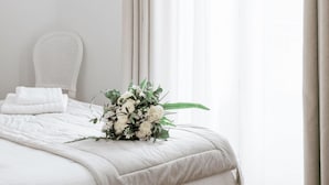 A neatly made bed with white linens, a white chair, and a bouquet of flowers on the bed. - Welcome to Arsene Gardens (TINTÉNIAC)