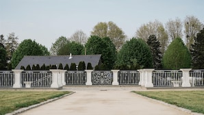 A gated entrance with a central pathway leading to a building with a dark roof. - Welcome to Arsene Gardens (TINTÉNIAC)