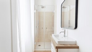 A modern bathroom with a glass-enclosed shower, a white sink, and a mirror on the wall. - Welcome to Arsene Gardens (TINTÉNIAC)