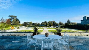 A patio with a round table and white metal chairs, surrounded by a stone pathway and a well-maintained garden. - Welcome to Arsene Gardens (TINTÉNIAC)