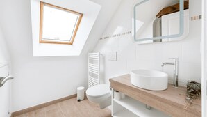 A modern bathroom with a skylight, a large mirror, and a white sink. - Welcome to Arsene Gardens (TINTÉNIAC)