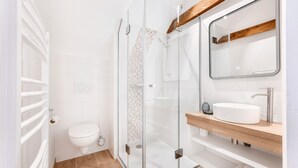 A modern bathroom with a glass shower enclosure, a white toilet, and a wooden vanity with a sink. - Welcome to Arsene Gardens (TINTÉNIAC)