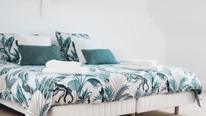 A bed with a tropical leaf pattern bedspread, white pillows, and neatly folded white towels. - Welcome to Arsene Gardens (TINTÉNIAC)