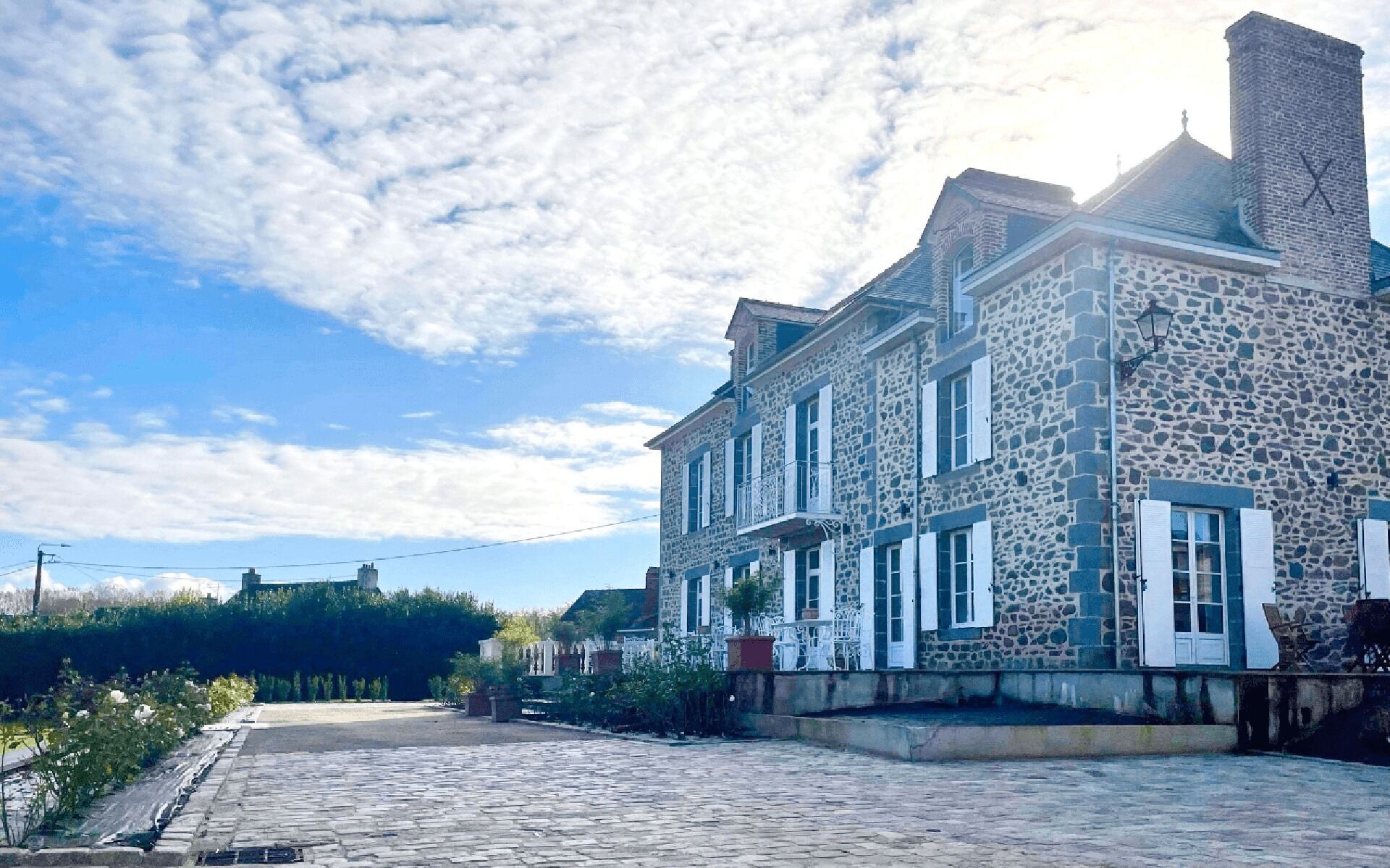 Un bâtiment en pierre, doté de nombreuses fenêtres et d’une cheminée, situé sur une rue pavée.