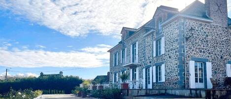 Un bâtiment en pierre, doté de nombreuses fenêtres et d’une cheminée, situé sur une rue pavée.