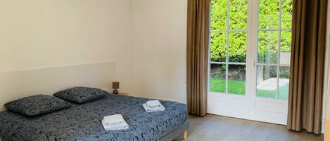 Ein Schlafzimmer mit einem Bett, zwei Kissen, einem Nachttisch und einem Fenster mit Vorhängen.