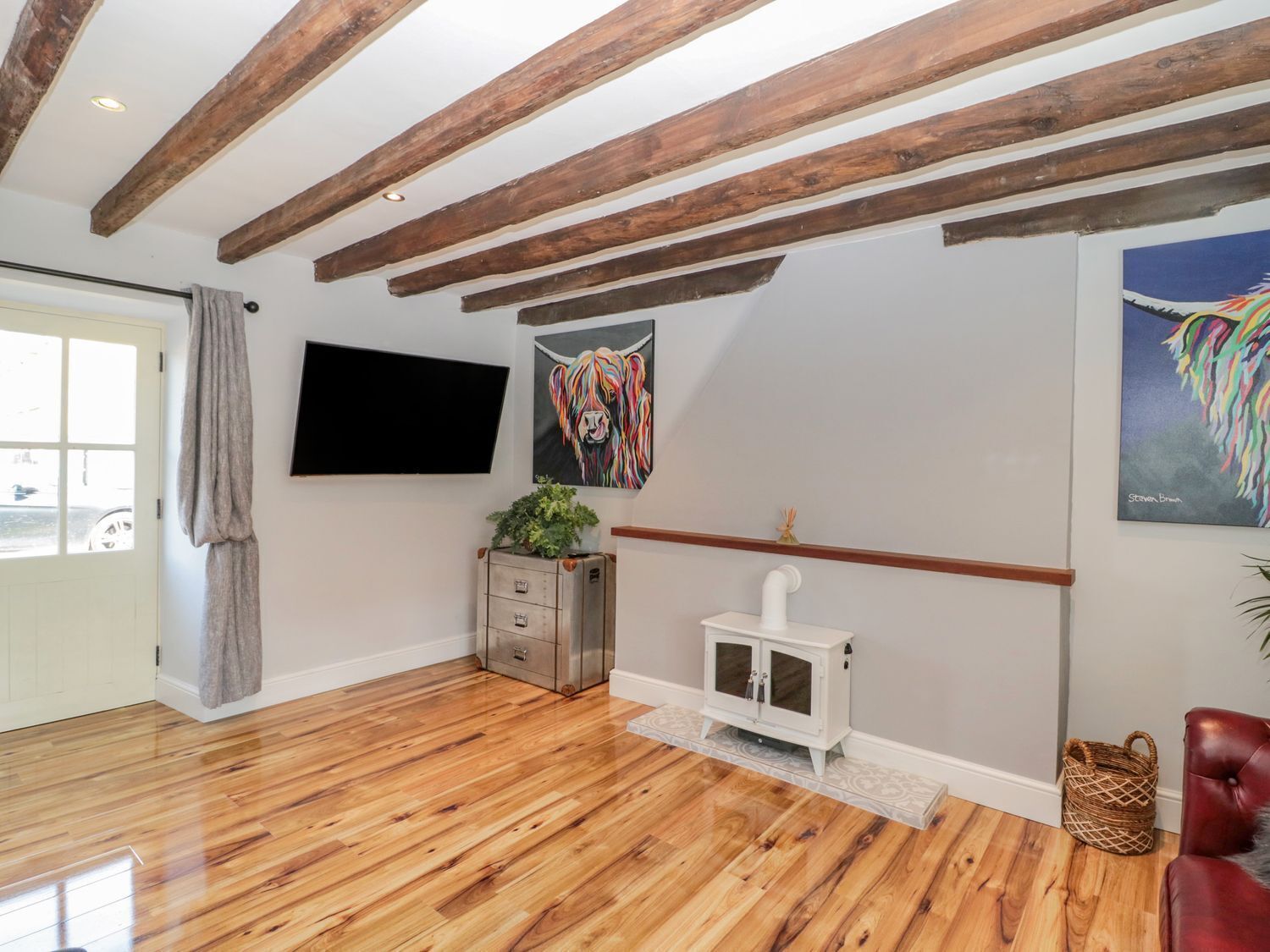 Una habitación con vigas de madera en el techo, un televisor de pantalla plana montado en la pared, un cuadro de un león colorido, un armario blanco y un sillón de cuero rojo.
