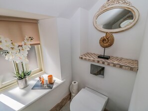 A bathroom with a window, a mirror, a toilet, and a shelf with decorative items. - O'neil Cottage (Chathill)