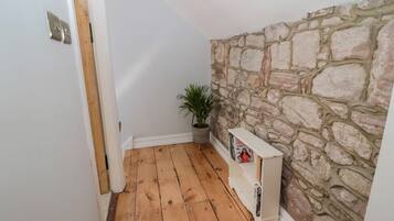 A narrow hallway with wooden flooring, a stone wall, and a white door.