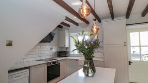 Une cuisine moderne avec des armoires blanches, un four encastré, un micro-ondes et un îlot central agrémenté d’un vase de fleurs.