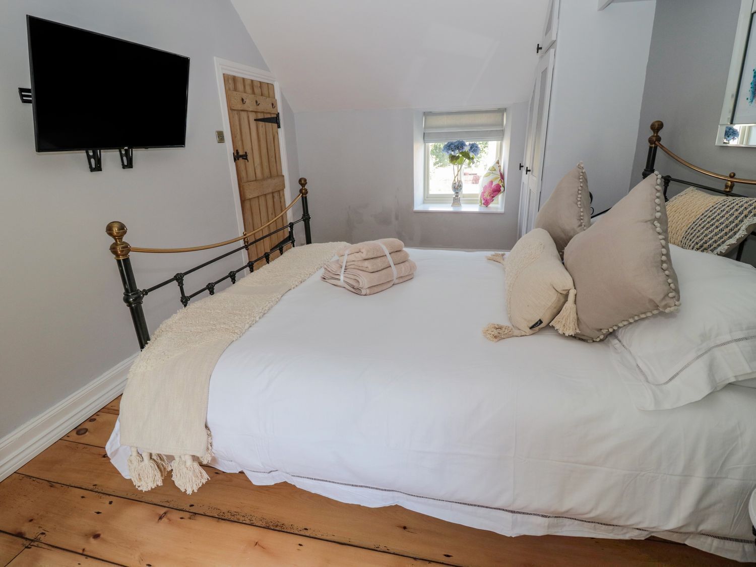 Un dormitorio con cama, televisor montado en la pared, ventana con vistas y puerta de madera.
