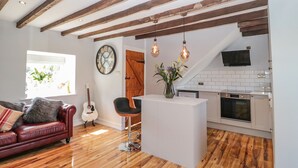 Un salon moderne avec des poutres en bois, un canapé blanc, une guitare et un coin repas avec une cuisine.