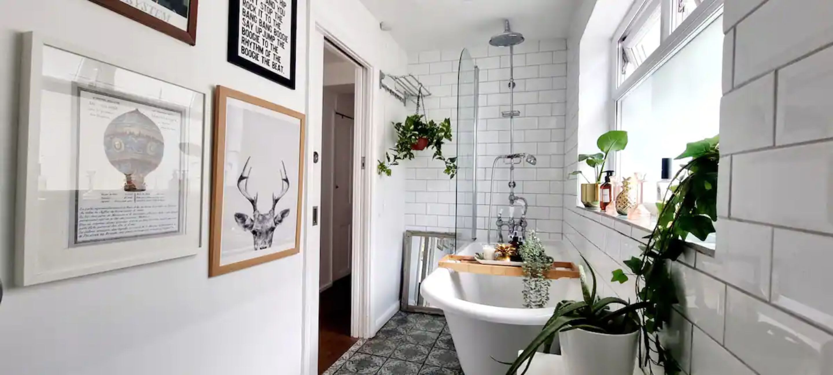 A narrow hallway with a white bathtub, framed artwork, and potted plants.