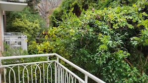 A balcony with white metal railings, surrounded by lush green foliage and a building with ivy-covered walls in the background. - Homely 1 Bedroom Retreat in South Yarra With Balcony (South Yarra)