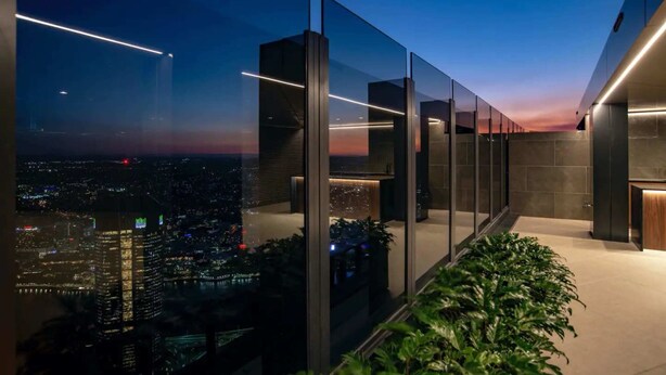 Un bâtiment moderne doté de grandes fenêtres en verre, offrant une vue sur le paysage urbain au crépuscule, et un escalier menant à un étage supérieur.