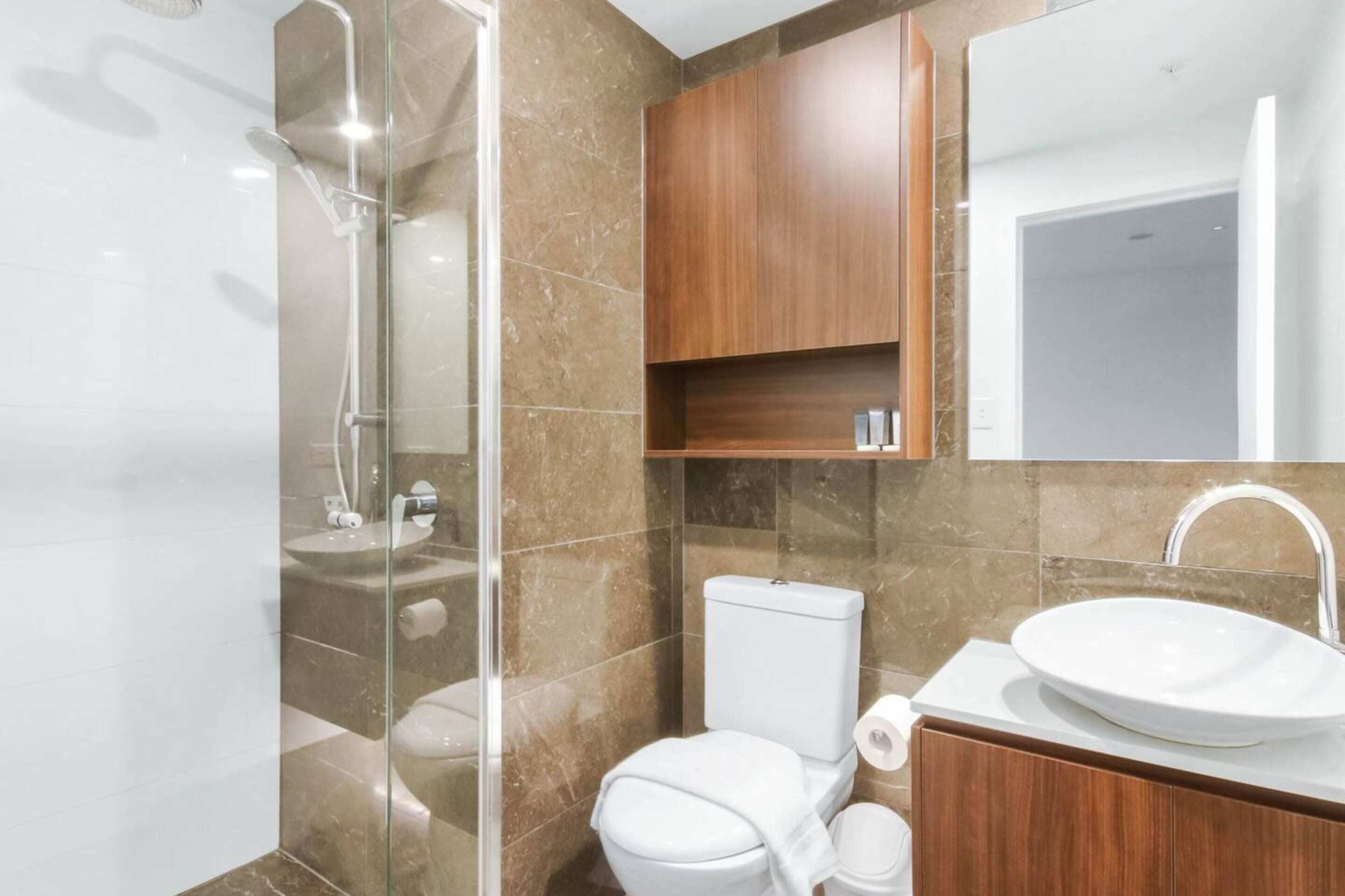 A modern bathroom with a glass-enclosed shower, a white toilet, a wooden vanity with a sink, and a mirror above the vanity.