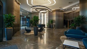 Un hall d’entrée moderne avec un plafond incurvé, de grandes plantes en pot et des sièges contemporains.