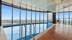 Une piscine intérieure moderne, dotée d’une terrasse en bois et de grandes fenêtres offrant une vue sur la ville.