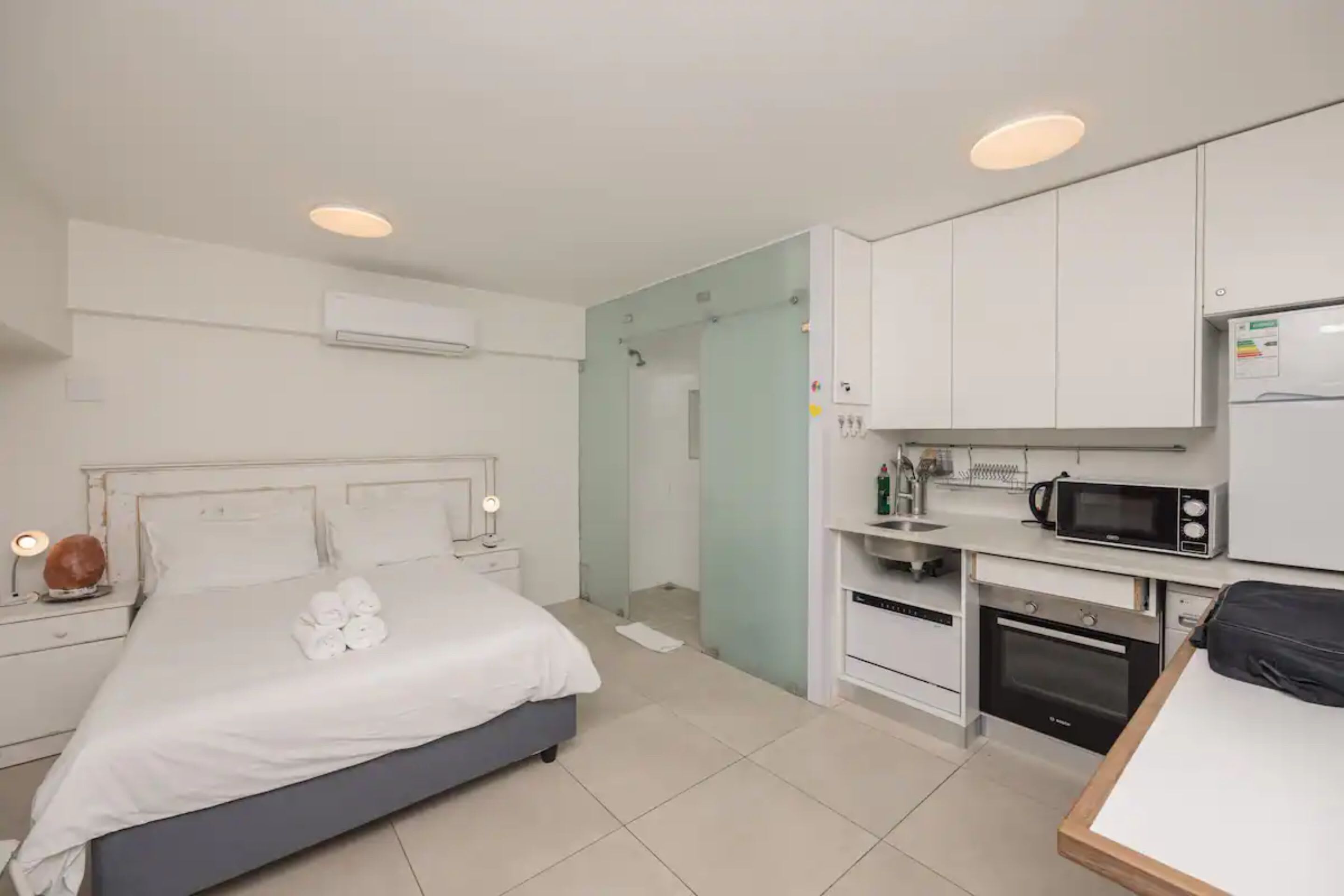 Ein modernes Hotelzimmer mit Bett, Nachttisch und einer Küchenzeile, einschließlich Mikrowelle und Backofen.