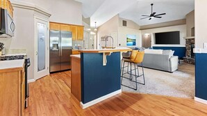 Una cocina moderna con una isla central, un área de comedor con un taburete de bar y una sala de estar con sofá y televisor.