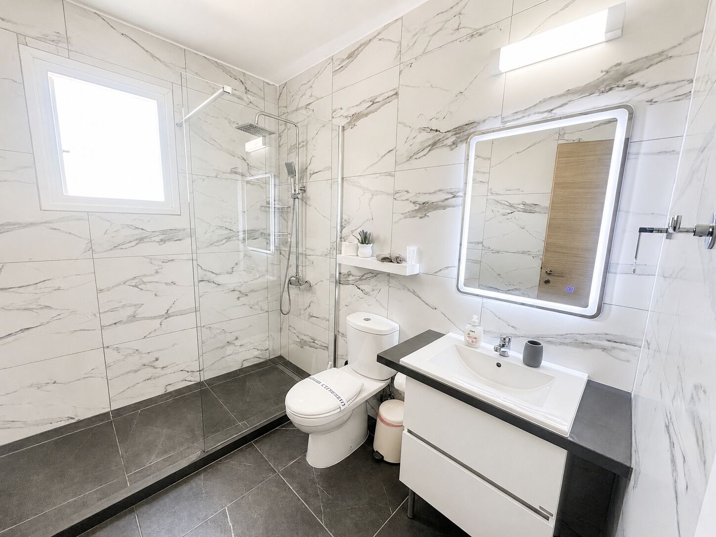 Ein modernes Badezimmer mit einer Duschkabine, einer Toilette, einem Waschbecken und einem Spiegel.