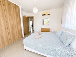 A bedroom with a bed, wardrobe, bedside table, and an air conditioning unit.