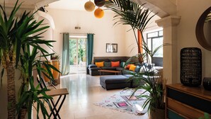 Een ruime woonkamer met een bank, een voetenbankje en grote planten.