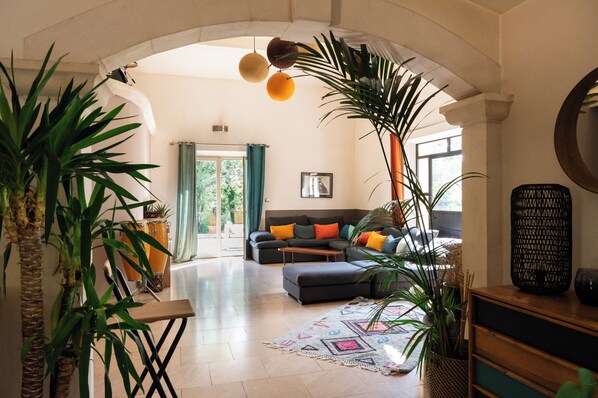 A spacious living room with a sofa, ottoman, and large plants.