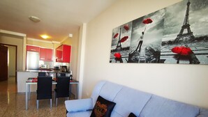Una sala de estar con un sofá, un comedor con sillas, una cocina y una pared decorada con un cuadro de París.