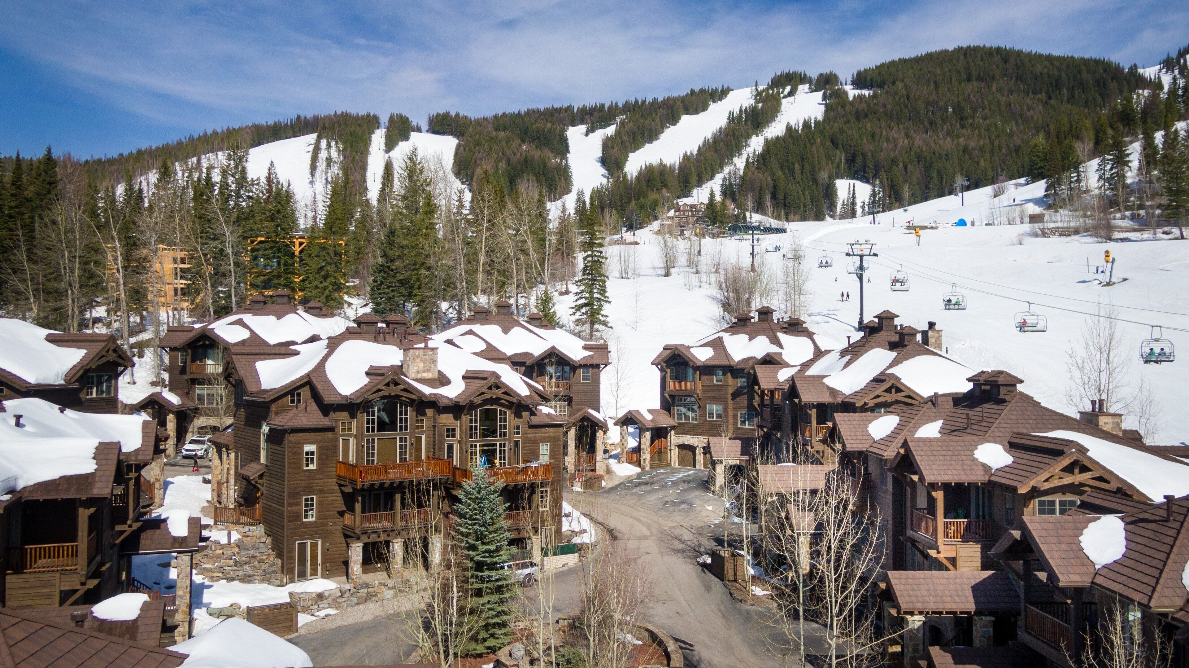 A ski resort with wooden buildings, a ski lift, and a snow-covered mountain.