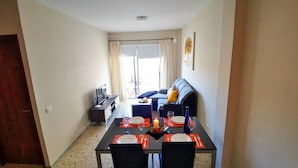 Un coin repas avec une table dressée pour quatre personnes, un canapé en arrière-plan et un téléviseur posé sur un meuble.