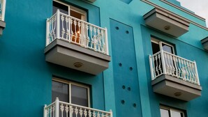 Un edificio con pareti esterne color acquamarina, balconi bianchi con ringhiere elaborate e una finestra circolare al livello superiore.