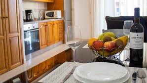 A kitchen with wooden cabinets, a microwave, and a dining table set with a wine glass, a plate, and a fruit basket.