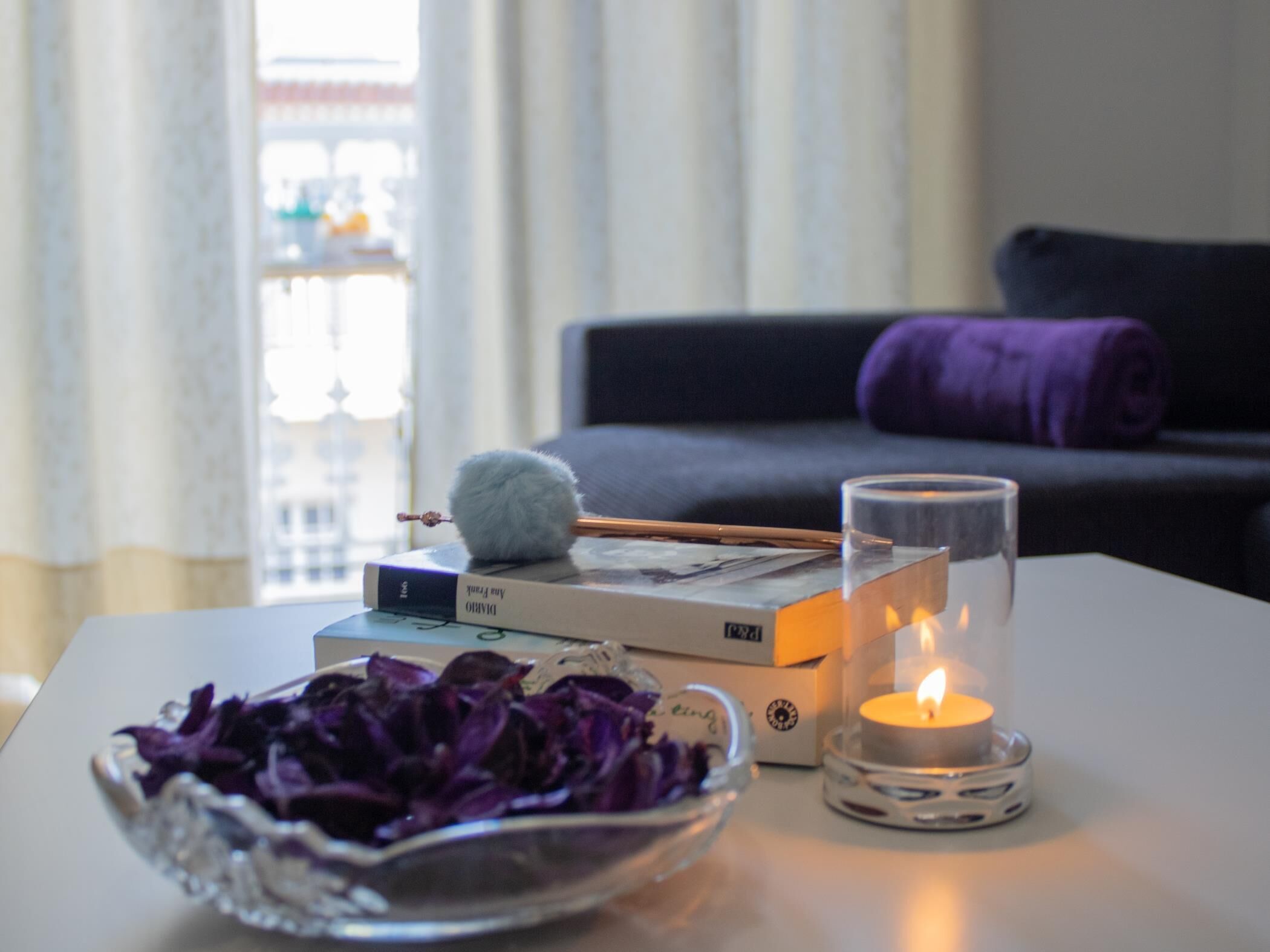 A table with a candle, a bowl of purple flowers, and books.