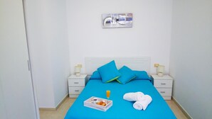 A hotel room with a bed, two bedside tables, a nightstand, a painting on the wall, and a tray with a drink and snacks on the bed. - PUESTA DE SOL RENTALS 2BR (PLAYA SAN JUAN)