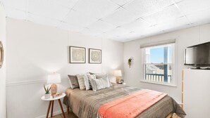 A bedroom with a bed, two bedside tables, a TV, and a window with a view. - Oceanfront condos with 3 night minimum rentals and linens included! (Ocean City)