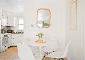 A modern kitchen with white cabinets, a microwave, stove, and a dining area with a white table and chairs. - Oceanfront condos with 3 night minimum rentals and linens included! (Ocean City)
