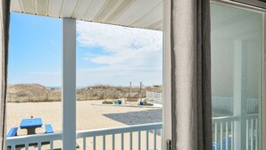 A beach view from a covered deck with a table and chairs. - Oceanfront condos with 3 night minimum rentals and linens included! (Ocean City)