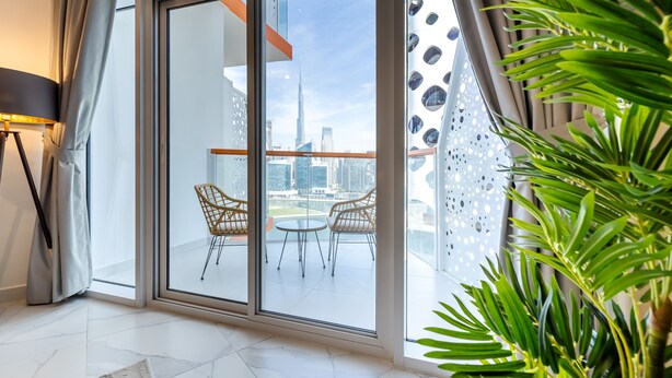 A modern living room with a large sliding glass door leading to a balcony with a city view. - Unlock Waters Edge (Dubai)