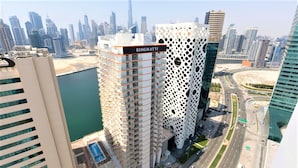 A modern high-rise building with a distinctive perforated facade, adjacent to a waterfront and a busy road. - Unlock Waters Edge (Dubai)