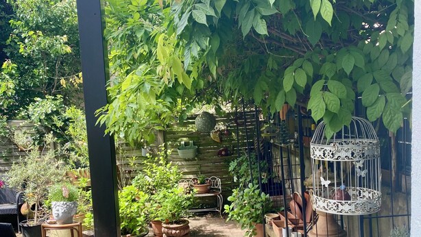 Un patio couvert agrémenté de plantes en pot, d’une cage à oiseaux et d’un sol en briques.