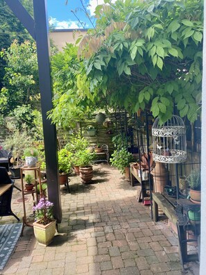 A covered patio area with potted plants, a birdcage, and a brick floor.