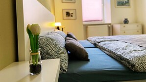 Une chambre à coucher avec un lit, des oreillers, une table de chevet, une lampe et un vase avec une fleur.