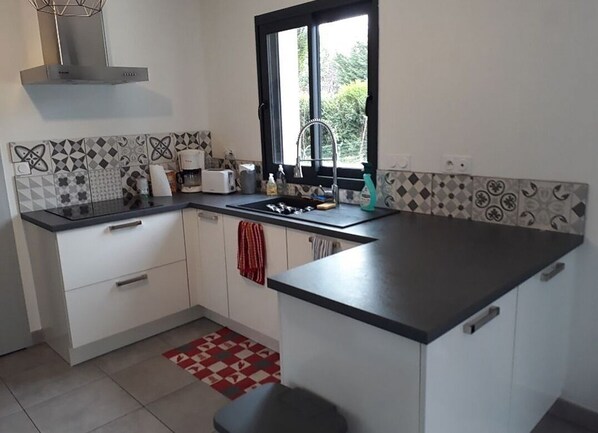 A kitchen with white cabinets, a black countertop, a window with a view, and a patterned backsplash. - Maison Neuve Proche Chinon (Beaumont-en-Véron)