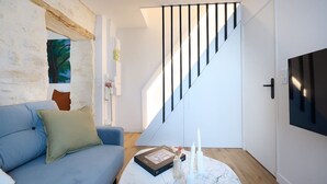 Una sala de estar moderna con un sofá azul, una mesa de centro de mármol y una escalera con barandillas negras.
