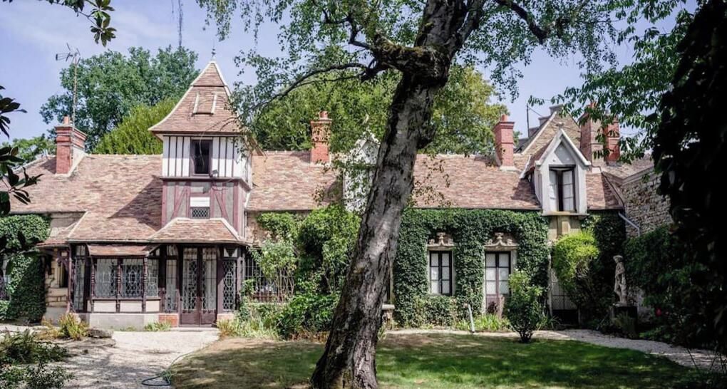 Una casa tradicional con una torre destacada, muros cubiertos de hiedra y un jardín bien cuidado.