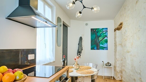 Una cocina moderna con extractor de acero inoxidable, una mesa redonda de comedor con sillas de vidrio transparente y un amplio ventanal que proporciona luz natural.