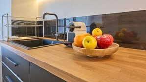 Una cocina con mostrador de madera, un lavamanos, un frutero con manzanas y naranjas, y una cafetera.