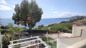 A balcony with a view of the sea, a parked car, and a large tree. - A terrace overlooking the sea 19084041C226886 (Sicilia)